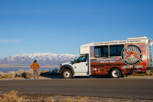 man with orange jacket, looking away from camera at mountains in the distance, shuttle bus to his right with antelope ebikes on it.